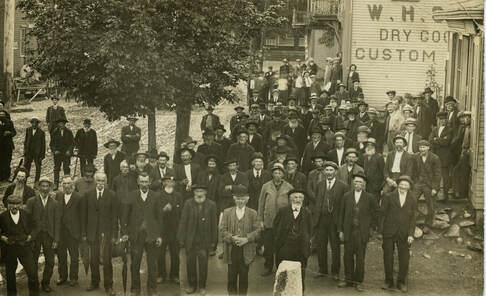 Sepia photo of a group of men standing on Main Street. A building with