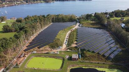 Image of solar panels on green grass with a blue sky with some clouds above.