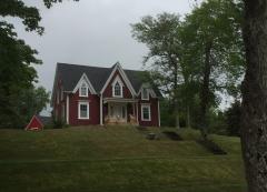 Red house on grassy hill surrounded by trees on a cloudy day.