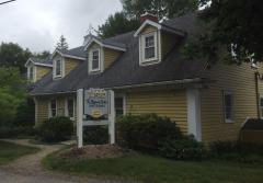 Yellow house with dormer windows, white trim, and a sign in the front yard.