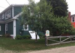 Green house with white trim, tree in front, wooden gate on grassy lawn.