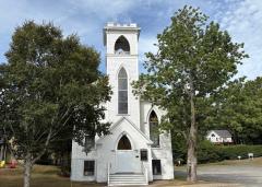 White church with tall steeple, surrounded by trees under a blue sky.