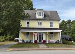 Yellow house with flags, red flowers, and trees nearby.