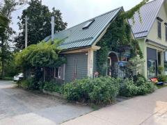 Small, green-roofed house with lush plants and vines in a suburban setting.