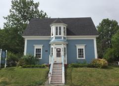 Blue house with a turret, surrounded by greenery.