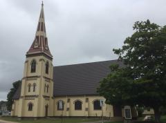 Steepled church with cloudy sky and large tree.