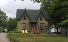 Charming small house with gabled roof, surrounded by trees, and colourful chairs in front.