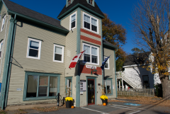 Historic building with Canadian flags, autumn trees, and bright blue sky.