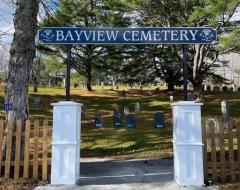 Bayview Cemetery entrance with tombstones under tall trees.