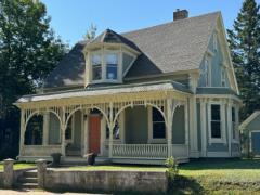 Victorian-style house with ornate porch, green lawn, and trees.