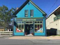 Bright blue shop with yellow trim, red flower pots, and Canadian flags in windows.